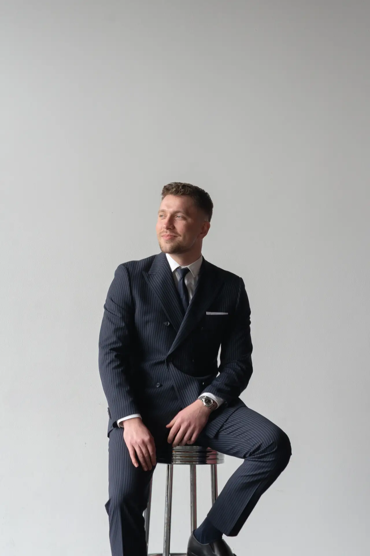 Broker Mark Datskiy on a stool in a pinstripe suit, looking aside.