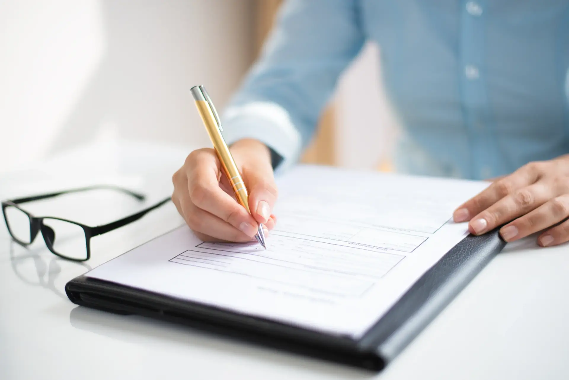 Woman signing home closing documents with a gold pen, with a Real Estate Broker in North Seattle.