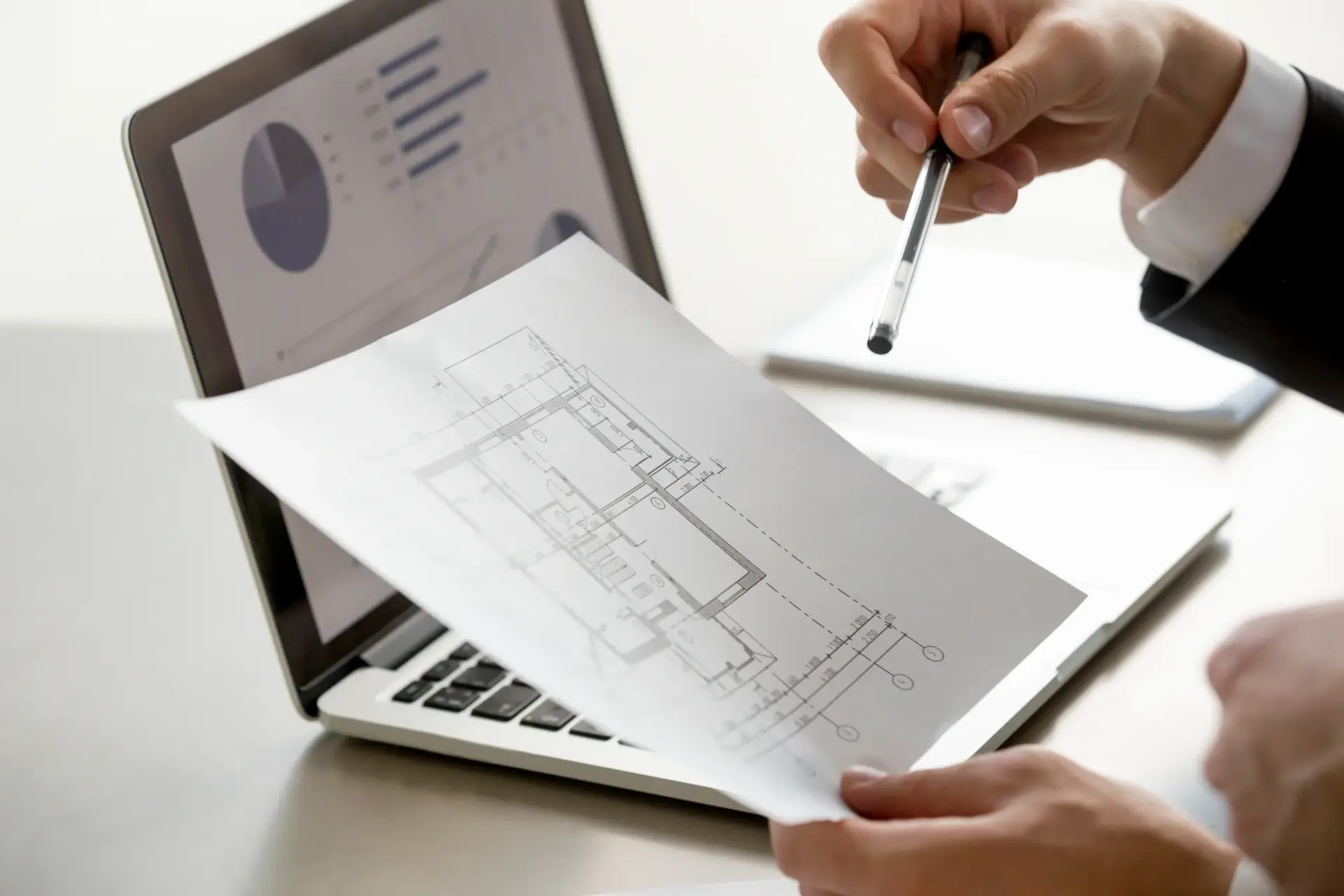 Person holding a floor plan over a laptop with charts to help Sell My House Fast North Seattle.