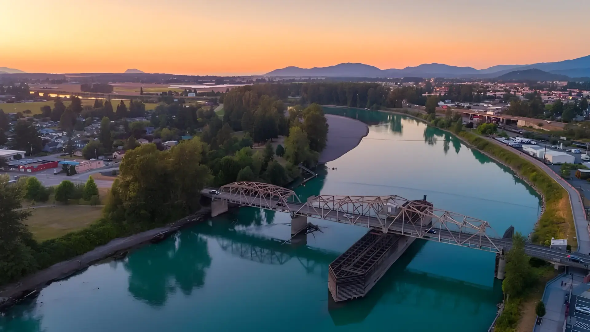Aerial view: A manufactured home is being towed on a barge down a river at sunset by a Real Estate Expert in Mount Vernon WA